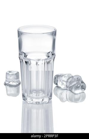 Leeres facettiertes Glas und drei Eiswürfel, die auf einem weißen Glastisch schmelzen Stockfoto