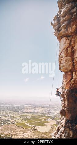 Person klettert auf eine Bergklippe für eine Herausforderung in der Natur mit blauem Himmel und Kopierraum. Klettererin auf einer Felswand für ein Fitnesstraining, Training und Sporttraining im Freien. Stockfoto