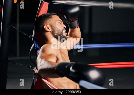 Müde Boxer, Fitness- und Sportwettkämpfe im Boxring, Entspannung während des mma-Kampfes und Atmung nach dem Wellness-Training im Fitnessstudio. Frustrierter Muay Thai-Athlet ohne Energie für das Workout Stockfoto