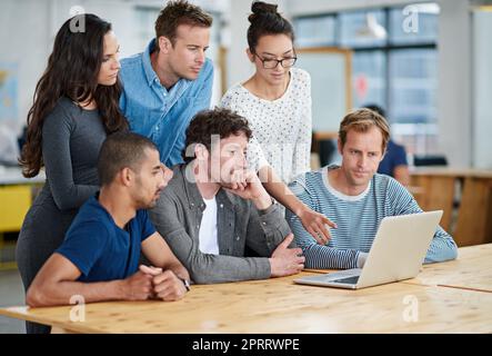 Viele Ideen auf den Tisch bringen: Eine Gruppe von Kollegen, die in einer zwanglosen Arbeitsumgebung einen Laptop verwenden. Stockfoto