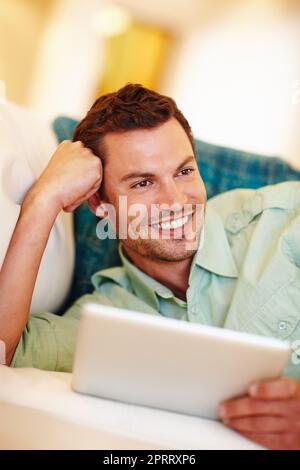 Fauler Nachmittag mit meinem E-Reader. Ein hübscher Mann, der sich mit seinem digitalen Tablet auf der Couch entspannt. Stockfoto