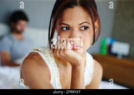 Probleme in der Beziehung. Eine verärgerte Frau sitzt auf der Seite ihres Bettes mit ihrem Freund im Hintergrund. Stockfoto