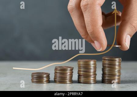 Konzept der Gehaltserhöhung. Frau, die Münzen auf einen grauen Tisch stapelt und Abbildung eines Aufwärtspfeils Stockfoto