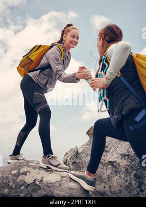 Wandern, Hilfe und Freunde auf einem Felsen- oder Bergsteigerabenteuer für Fitness, Bewegung und Adrenalin. Glückliche Frauen mit Unterstützung, Reisen und Hilfe, während sie auf der Klippe sind und den Gipfel erreichen Stockfoto