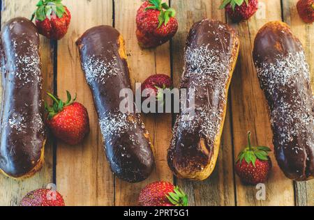 Schokoladen-Profiteroles und frische Erdbeeren auf einem Holztisch Stockfoto