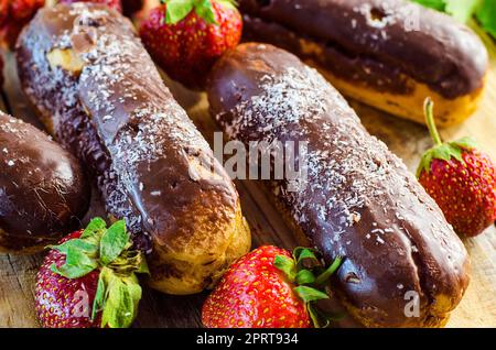 Schokoladen-Profiteroles und frische Erdbeeren auf einem Holztisch Stockfoto