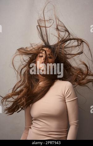 Schmutzige Haare, ist mir egal. Porträt einer wunderschönen jungen Frau, die im Studio mit dem Wind im Haar posiert Stockfoto