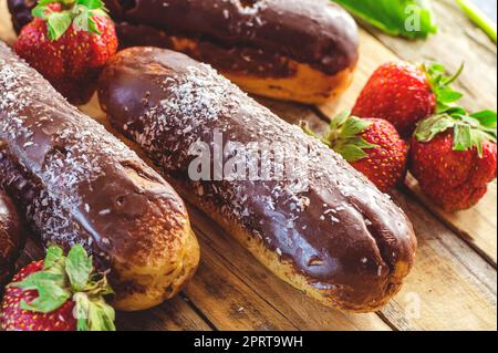 Schokoladen-Profiteroles und frische Erdbeeren auf einem Holztisch Stockfoto