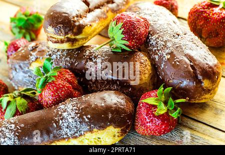 Schokoladen-Profiteroles und frische Erdbeeren auf einem Holztisch Stockfoto