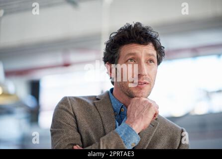 HES hat die Zukunft perfekt geplant. Porträt eines gutaussehenden Mannes, der in Gedanken wegschaut und hinter ihm einen industriellen Raum hat. Stockfoto