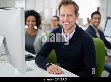 Unser Arbeitsplatz hat eine positive Einstellung. Porträt eines lächelnden Geschäftsmannes mit seinen Mitarbeitern im Hintergrund. Stockfoto