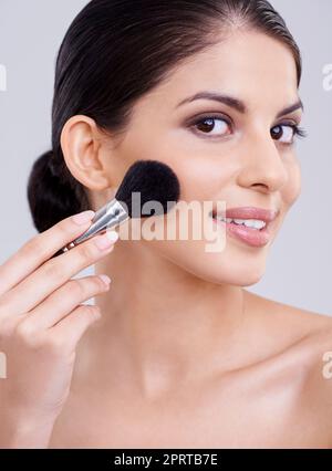 Ihre Wangen sind schön und rosig. Eine schöne junge Frau, die ihr Gesicht mit Blusher bestülpst. Stockfoto