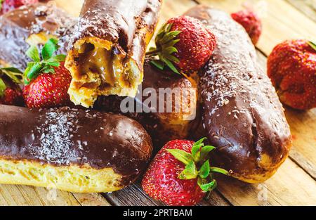 Schokoladen-Profiteroles und frische Erdbeeren auf einem Holztisch Stockfoto