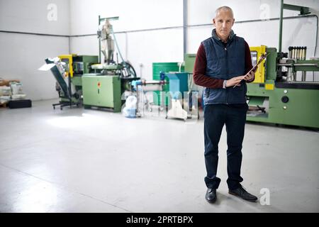 HES hat alles unter Kontrolle. Porträt eines männlichen Vorarbeiters, der mit einem Klemmbrett auf der Fabriketage steht. Stockfoto