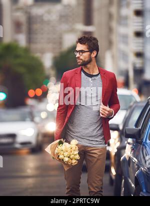 Stoppen Sie den Verkehr mit Ihrem Charme und Aussehen. Ein hübscher junger Mann, der auf der Straße mit Autos hinter ihm mit einem Blumenstrauß geht. Stockfoto