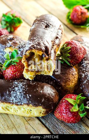 Schokoladen-Profiteroles und frische Erdbeeren auf einem Holztisch Stockfoto