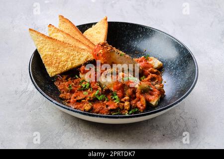 Gebratener Zander serviert mit gedämpfter Tomaten-, Zwiebeln- und Olivensauce Stockfoto