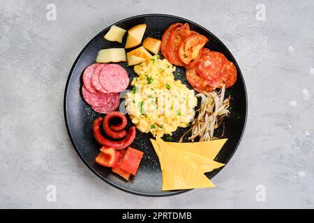 Draufsicht auf einen Teller mit Rührei mit verschiedenen Würstchen, Käse, Paprika und gerösteten Zwiebeln Stockfoto