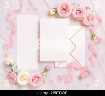 Leere Papierkarten zwischen pinkfarbenen Rosen und pinkfarbenen Seidenbändern auf pinkfarbener Draufsicht, Hochzeitsmodell Stockfoto