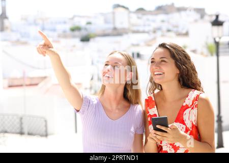 Zwei glückliche Touristen, die in einer Stadt auf ihr Handy zeigen Stockfoto
