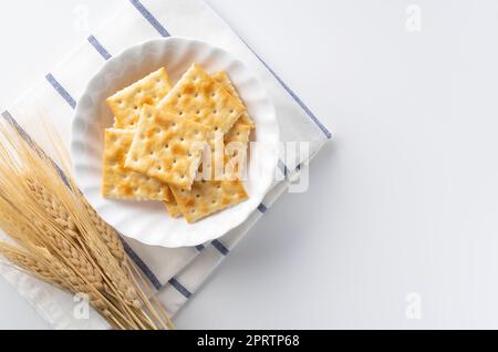 Viele Cracker auf einer Platte, die auf einem weißen Hintergrund mit Platz platziert ist. Blick von direkt oben. Stockfoto