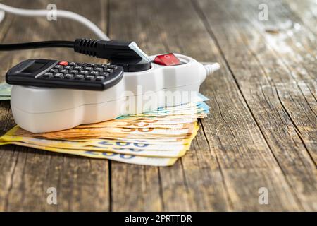 Elektrostecker, Taschenrechner und Euro-Geld auf Holztisch. Konzept steigender Strompreise. Stockfoto