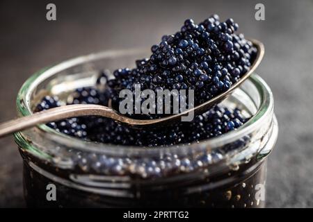 Schwarzer Kaviar in silbernem Löffel auf dunklem Tisch. Stockfoto