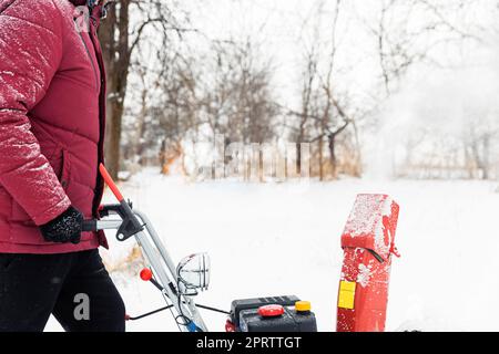 Mann mit roter Schneefräse im Freien. Schnee in der Nähe des Hauses vom Hof entfernen Stockfoto