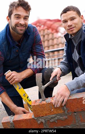 Diese Mauer wird stark sein. Porträt eines Maurersoluns und seines Lehrlings bei der Arbeit. Stockfoto