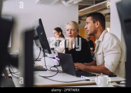 Weibliche, ausgereifte Professorin mit Doktoranden, die Computer im Innovationslabor benutzt Stockfoto