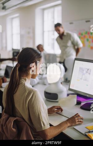 Seitenansicht einer Studentin, die am Schreibtisch sitzt und den Computer benutzt Stockfoto