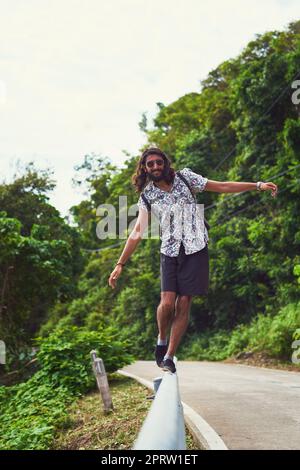 Auf der Suche nach der weniger befahrenen Straße. Porträt eines glücklichen jungen Mannes, der ein exotisches Reiseziel allein erforscht Stockfoto