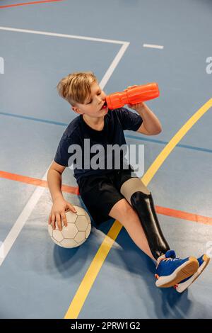 Aus dem Blickwinkel des männlichen Sportlers, der nach einem Fußballspiel auf dem Sportplatz Wasser trinkt Stockfoto
