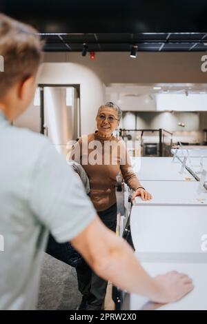 Seniorin, die mit einem Verkäufer spricht, indem sie Waschmaschinen im Elektronikgeschäft betreibt Stockfoto