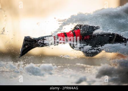 Nahaufnahme der Hand, die einen Schneeschaber hält und Eis von der Windschutzscheibe entfernt Stockfoto