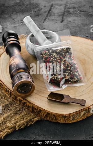 Holzquerschnitt mit Gemisch aus Paprika in Kunststoffverpackung, Mörtel und Mühle Stockfoto