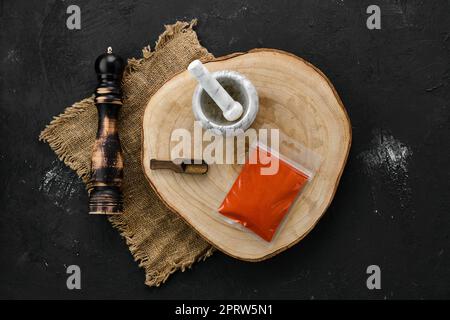 Holzquerschnitt mit geräucherter Paprika in Kunststoffverpackung und Mörtel und Mühle Stockfoto