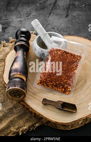 Holzquerschnitt mit Chiliflocken in Kunststoffverpackung und Mörtel und Mühle Stockfoto