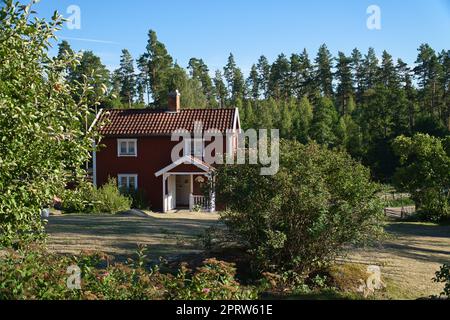 Traditionelles schwedisches rot-weißes Haus in Smalland, weißer Zaun, grüner Garten, blauer Himmel Stockfoto