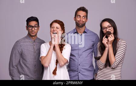 Lassen Sie uns etwas Humor in ihn stecken. Studioaufnahme einer Gruppe verschiedener junger Menschen vor grauem Hintergrund. Stockfoto