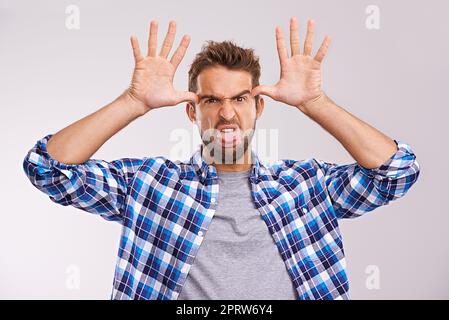 Fügen Sie einige albern zu Ihrem Tag. Ein junger Mann, der ein Gesicht vor einem grauen Hintergrund macht. Stockfoto