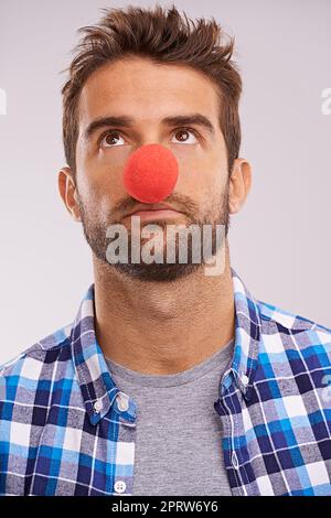 Herumclowning. Studioaufnahme eines hübschen Mannes mit roter Nase vor grauem Hintergrund. Stockfoto