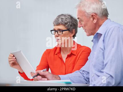 Ihre Erfahrung macht den Unterschied: Zwei reife Kollegen sitzen mit einem digitalen Tablet und diskutieren über die Arbeit. Stockfoto