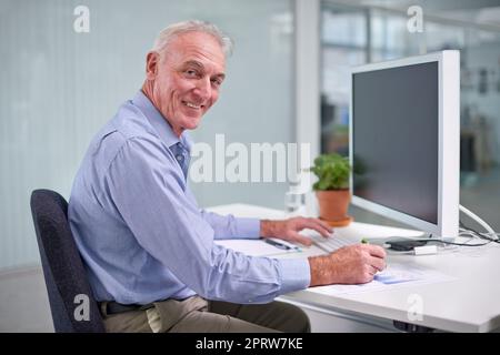 HES das Beste im Unternehmen. Porträt eines reifen Geschäftsmannes, der an seinem Schreibtisch arbeitet. Stockfoto