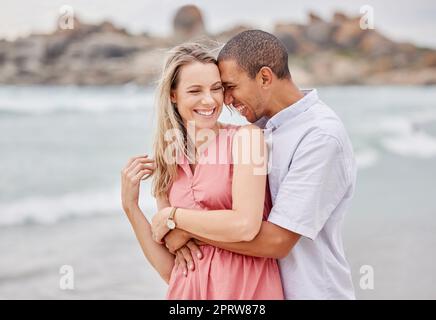 Reisen, Strand und Paare umarmen, glücklich und lachen, während sie sich im Freien anfreunden und den Blick auf das Meer genießen. Liebe, Beziehung und Wasserspaß mit Mann und Frau auf einem Strandausflug in San francisco Stockfoto