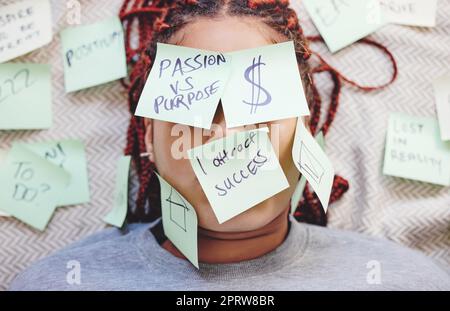 Schwarze Frau müde mit Haftnotiz im Gesicht, Motivation zum Erfolg und Geld im Bett. Afrikanisches Mädchen im Schlafzimmer, Ideen auf Haut und Augen kleben, um Träume von Haus und Wohlstand zu manifestieren Stockfoto