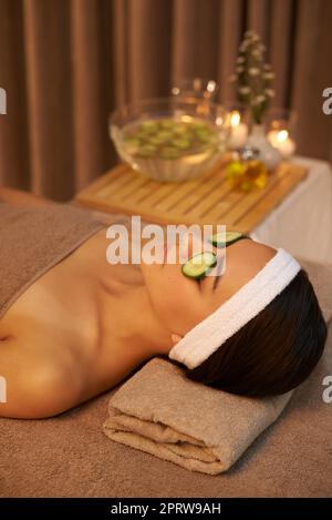 Lassen Sie die Gurken ihre Magie wirken. Eine schöne junge Frau, die auf einem Massageliegen im Spa mit Gurken über den Augen liegt. Stockfoto