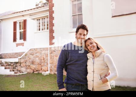 Wir träumten immer davon, ein Haus zu besitzen, und jetzt tun wir es. Eine beschnittene Ansicht eines Ehepaares, das im Vorgarten steht. Stockfoto