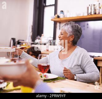 Einfach unvergleichlich... eine hausgemachte Mahlzeit. Eine glückliche ältere Frau, die mit ihrer Familie zu Hause ein Essen teilt. Stockfoto