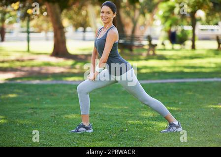 Dehnung schmerzende Muskeln. Ganzkörperaufnahme einer Frau, die sich vor ihrem Lauf im Park ausdehnt. Stockfoto